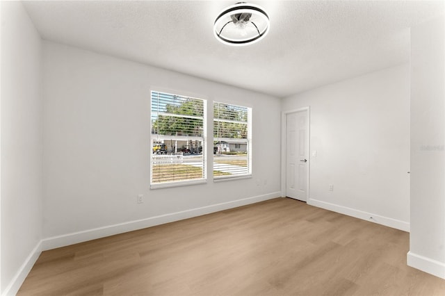 empty room with light wood-style floors, baseboards, and a textured ceiling