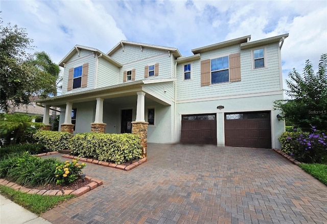 craftsman-style home featuring stucco siding, decorative driveway, a porch, and a garage
