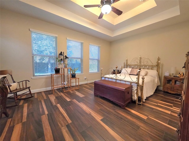 bedroom featuring baseboards, a tray ceiling, multiple windows, and wood finished floors
