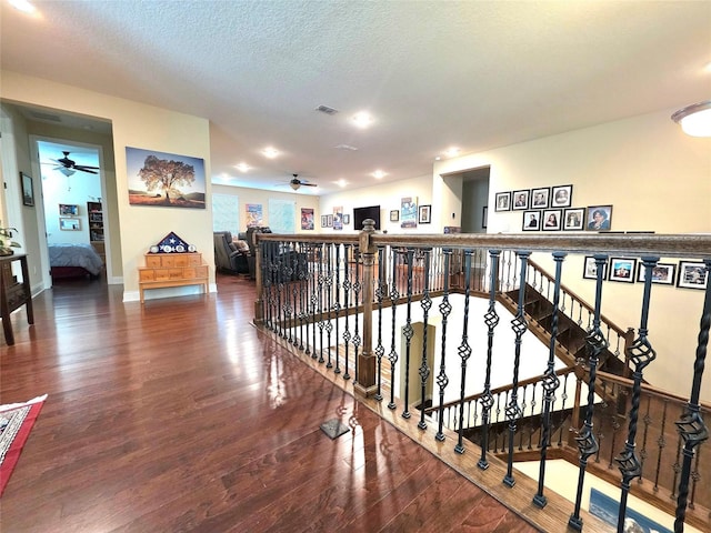 hall featuring a textured ceiling, an upstairs landing, wood finished floors, and visible vents