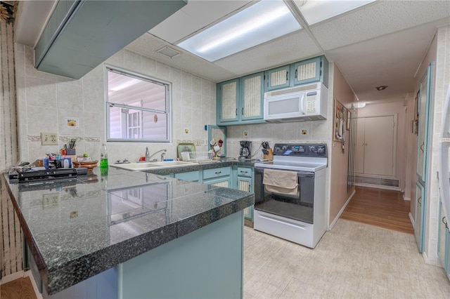 kitchen with a sink, light wood-style floors, tile countertops, white appliances, and a peninsula