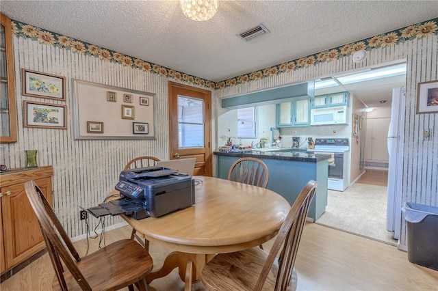 dining area with a textured ceiling, visible vents, wallpapered walls, and light wood-style flooring
