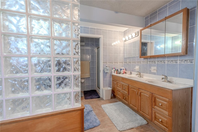 full bath with tile patterned flooring, double vanity, tile walls, a sink, and a stall shower