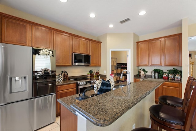 kitchen featuring stainless steel appliances, a kitchen breakfast bar, a sink, dark stone countertops, and brown cabinets