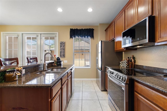kitchen featuring a sink, dark stone countertops, light tile patterned flooring, brown cabinets, and appliances with stainless steel finishes