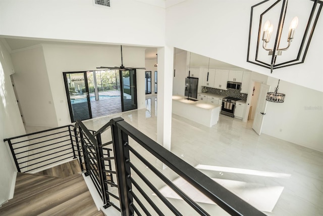 stairs with ceiling fan, a chandelier, and a high ceiling