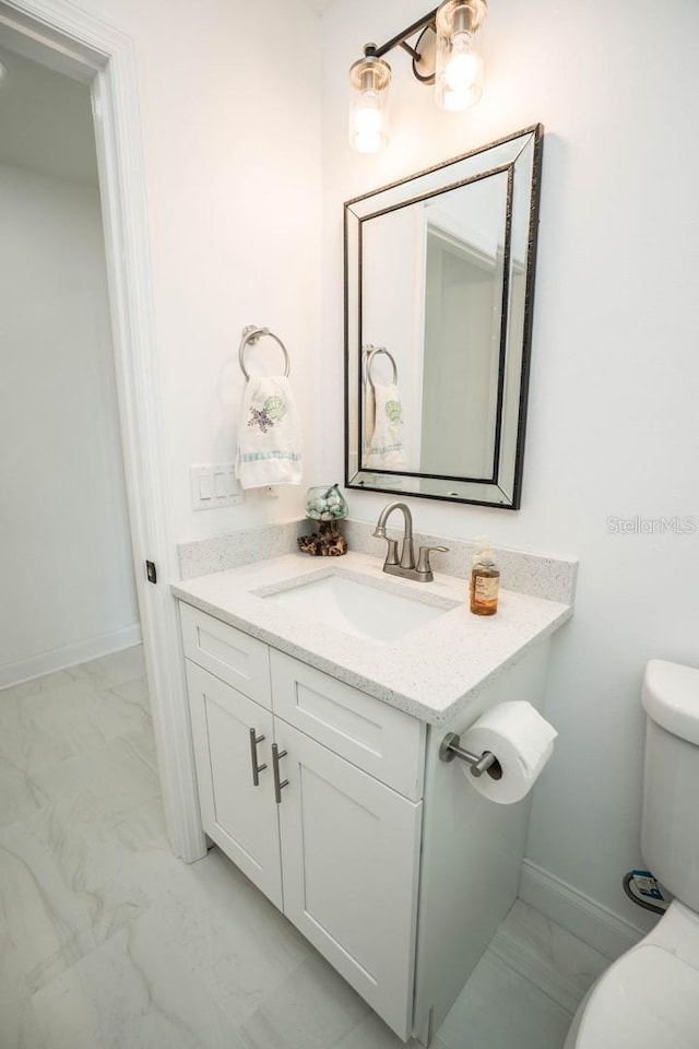 half bath with marble look tiles, toilet, vanity, and baseboards