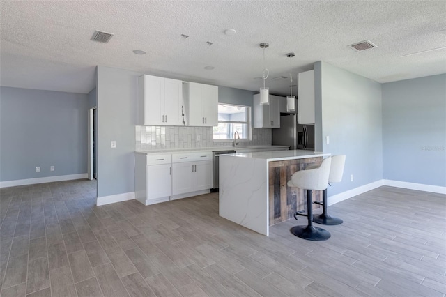 kitchen with light wood finished floors, visible vents, a kitchen island, appliances with stainless steel finishes, and a breakfast bar area