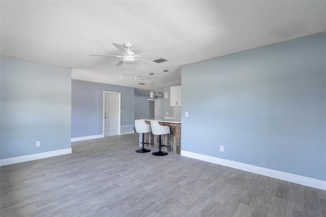 unfurnished living room with baseboards, a ceiling fan, wood finished floors, and visible vents