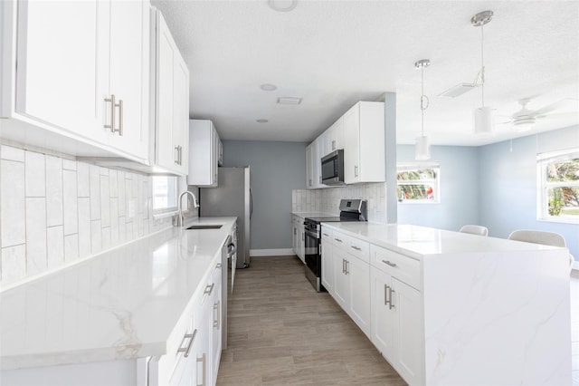 kitchen featuring a sink, light wood-style flooring, backsplash, a peninsula, and appliances with stainless steel finishes