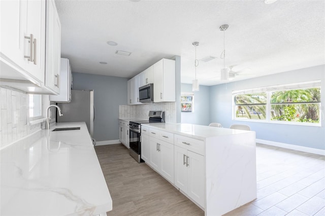 kitchen with tasteful backsplash, a sink, baseboards, a peninsula, and appliances with stainless steel finishes