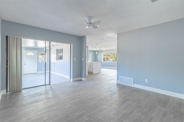 interior space with ceiling fan with notable chandelier, baseboards, light wood-style flooring, and visible vents