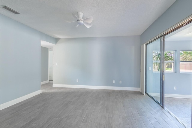 empty room featuring wood finished floors, visible vents, a ceiling fan, and baseboards