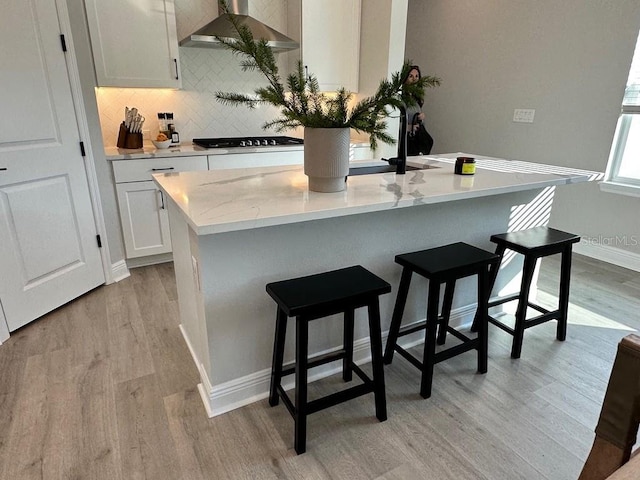 kitchen with light wood finished floors, wall chimney exhaust hood, black cooktop, tasteful backsplash, and a breakfast bar