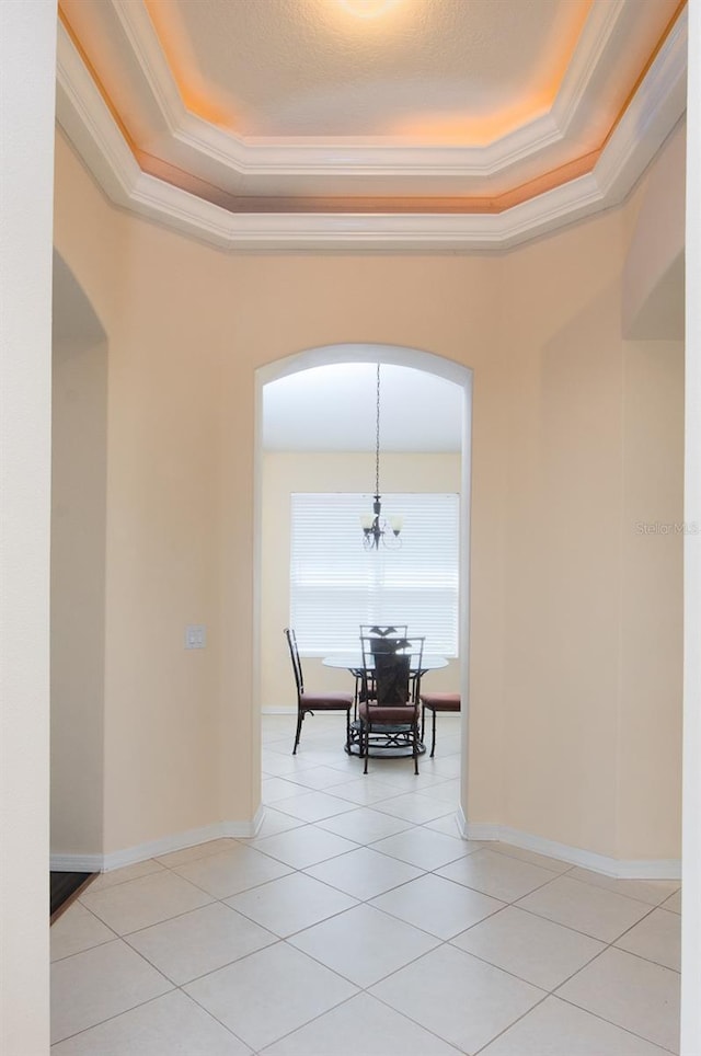 spare room featuring a raised ceiling, arched walkways, crown molding, light tile patterned floors, and baseboards