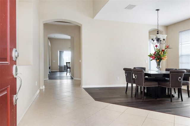 dining room featuring arched walkways, a chandelier, tile patterned floors, and baseboards