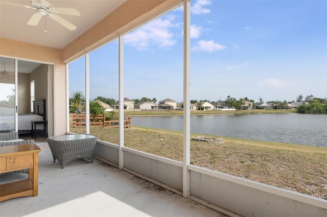 sunroom featuring a ceiling fan, a water view, and a residential view