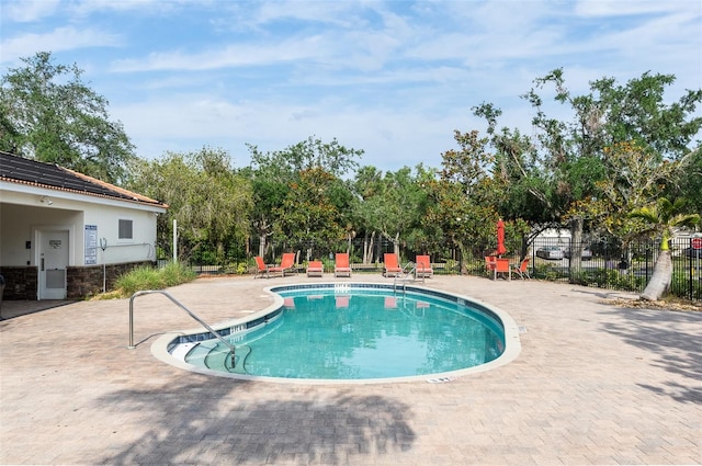 community pool featuring fence, a patio, and view of wooded area