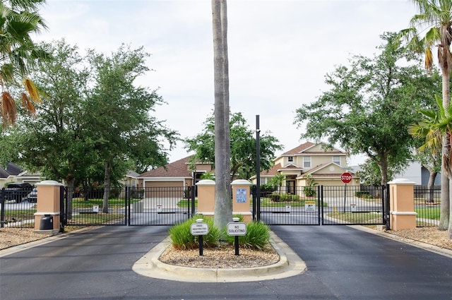view of asphalt street featuring traffic signs, a gate, curbs, and a gated entry