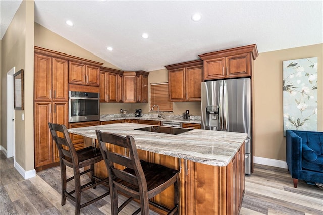 kitchen with stainless steel appliances, a kitchen island, brown cabinetry, and baseboards
