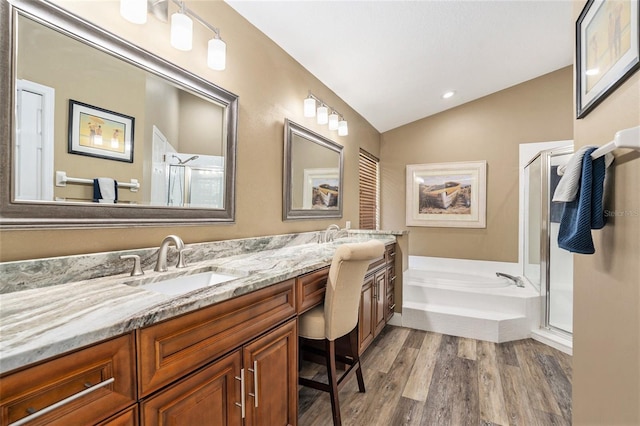 full bathroom with wood finished floors, double vanity, vaulted ceiling, a sink, and a stall shower