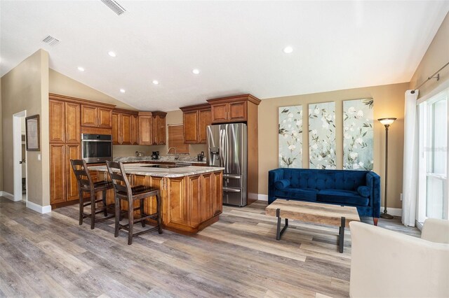 kitchen featuring appliances with stainless steel finishes, brown cabinets, light wood-style flooring, and lofted ceiling