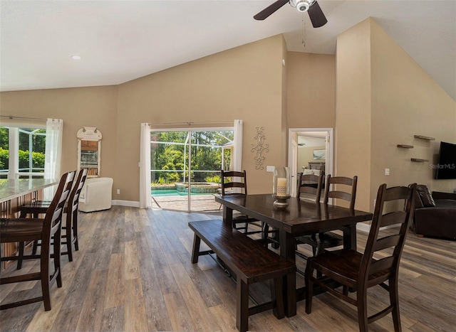 dining space with baseboards, high vaulted ceiling, wood finished floors, and a ceiling fan