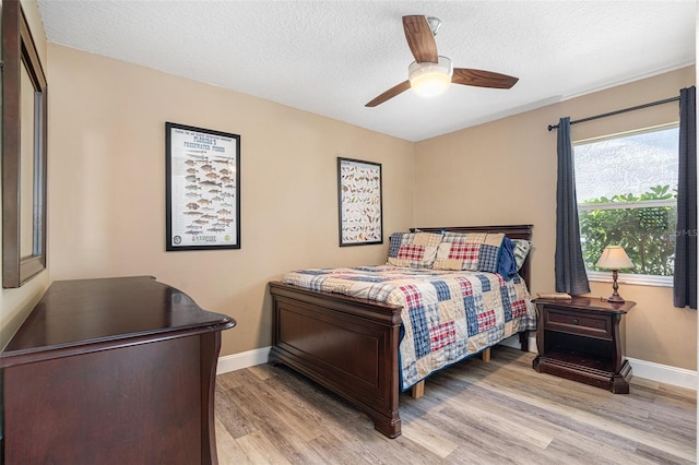 bedroom featuring baseboards, light wood-type flooring, a ceiling fan, and a textured ceiling
