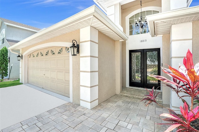 property entrance featuring an attached garage, driveway, stucco siding, and french doors