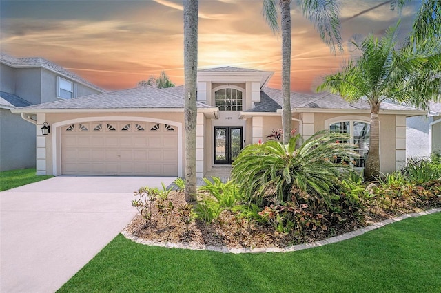 view of front of property featuring a front yard, a garage, driveway, stucco siding, and french doors