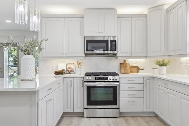 kitchen featuring light wood-style flooring, stainless steel appliances, decorative light fixtures, backsplash, and a peninsula