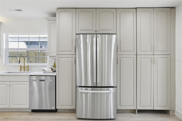 kitchen with a sink, light wood-type flooring, visible vents, light countertops, and appliances with stainless steel finishes