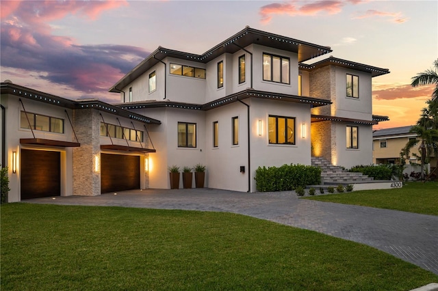 mediterranean / spanish house featuring an attached garage, a lawn, stucco siding, and decorative driveway