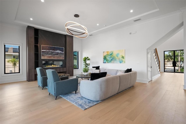 living room with a tray ceiling, light wood-type flooring, baseboards, and ornamental molding