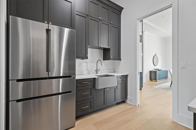 kitchen with light countertops, a sink, freestanding refrigerator, baseboards, and light wood-style flooring