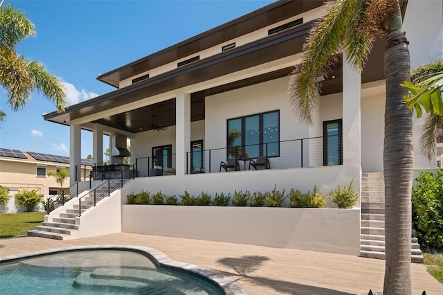 rear view of property with an outdoor pool, a ceiling fan, stairs, and stucco siding