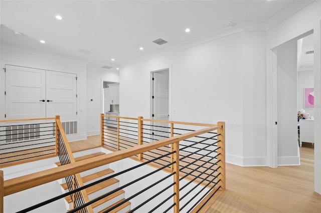 corridor featuring light wood finished floors, visible vents, an upstairs landing, crown molding, and baseboards