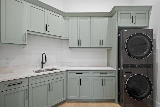 laundry area featuring stacked washer / drying machine, a sink, light wood finished floors, and cabinet space