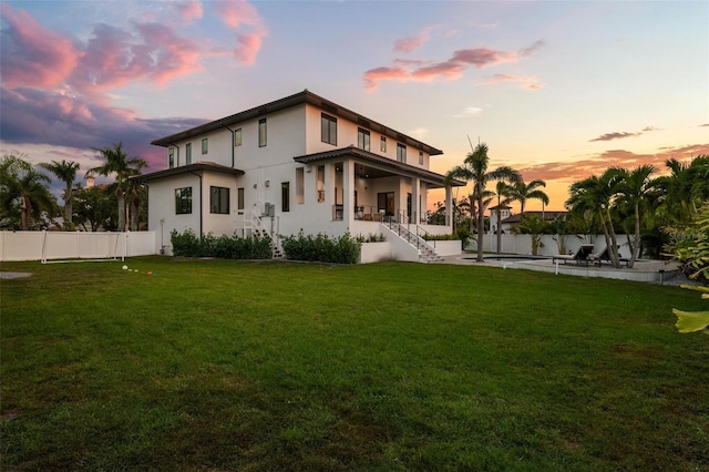 rear view of house with stairway, stucco siding, fence private yard, covered porch, and a lawn