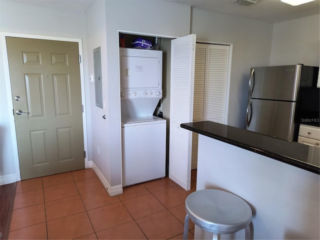 clothes washing area featuring laundry area, visible vents, stacked washer / drying machine, electric panel, and light tile patterned floors