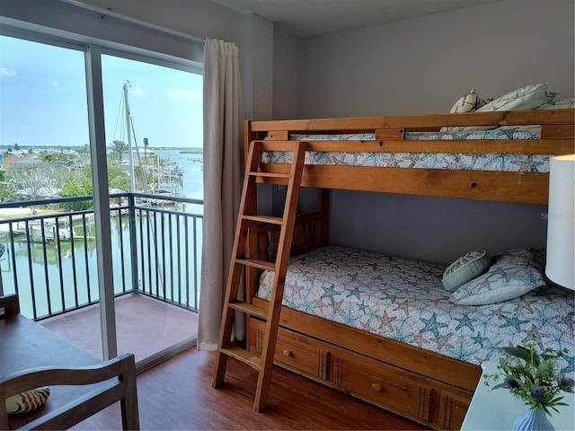 bedroom with a water view, access to outside, and wood finished floors