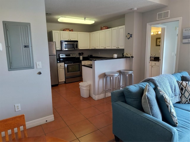 kitchen with light tile patterned flooring, stainless steel appliances, open floor plan, visible vents, and electric panel