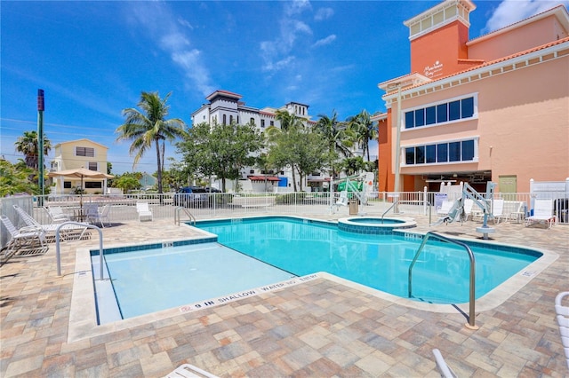 community pool with a patio area, a hot tub, and fence