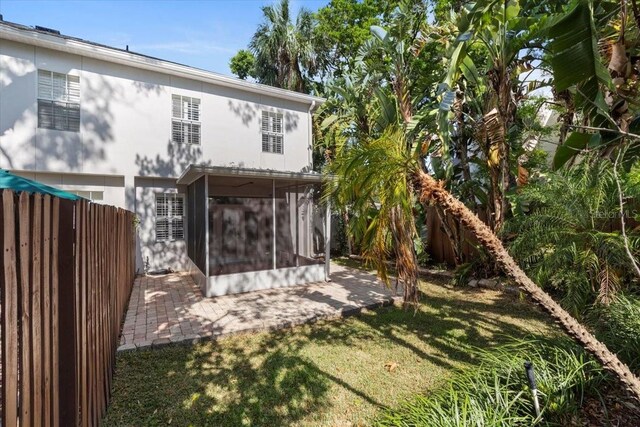 rear view of house featuring a sunroom, a patio area, fence, and a yard