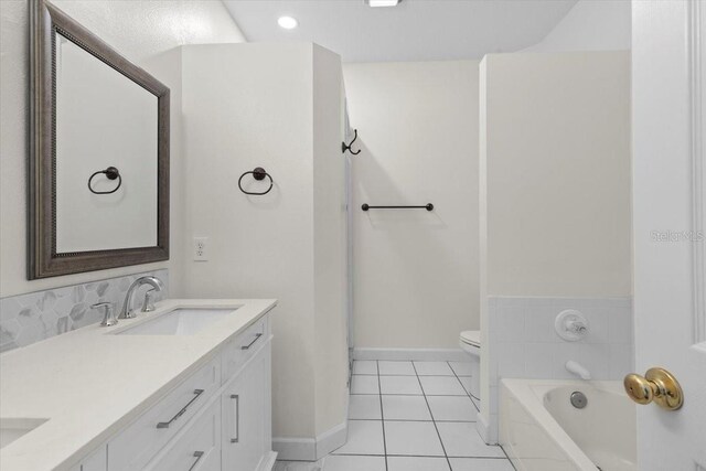 bathroom with toilet, baseboards, tile patterned floors, a tub to relax in, and a sink
