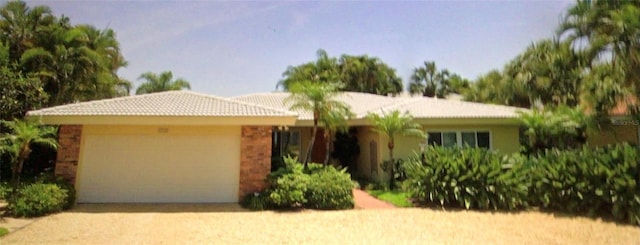 single story home featuring brick siding, an attached garage, a tiled roof, and driveway