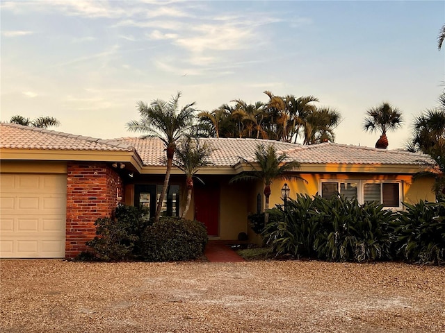 ranch-style home featuring a tiled roof, dirt driveway, an attached garage, and stucco siding
