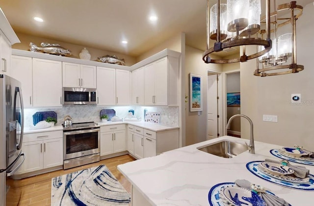 kitchen with a sink, white cabinetry, light wood-style flooring, appliances with stainless steel finishes, and light stone countertops