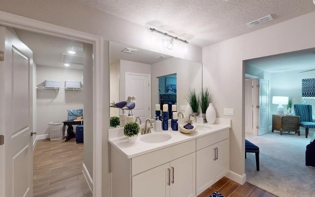 full bath with a sink, a textured ceiling, double vanity, visible vents, and wood finished floors