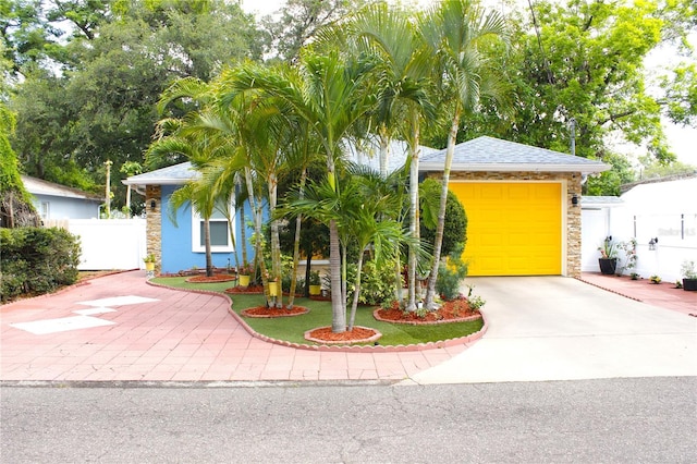 view of property hidden behind natural elements with fence, driveway, and stone siding